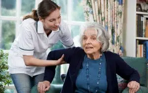 une aide à domicile et une personne agée dans un fauteuil dans son salon de sa maison